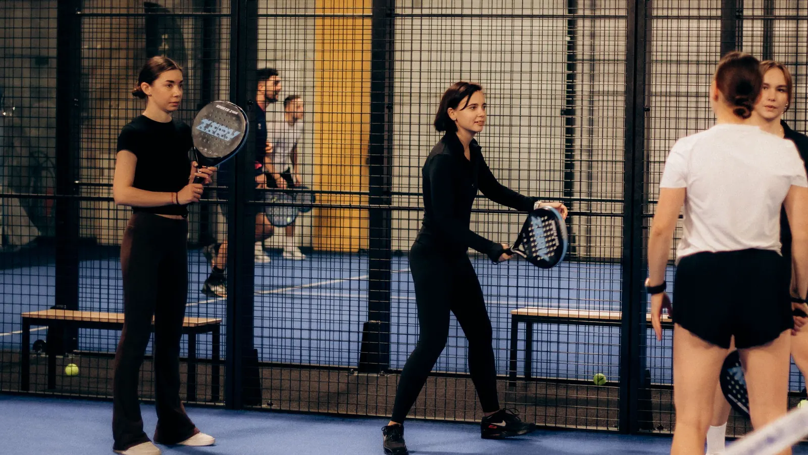 Quatre jugadors escalfant en una pista de pàdel coberta abans d'un partit